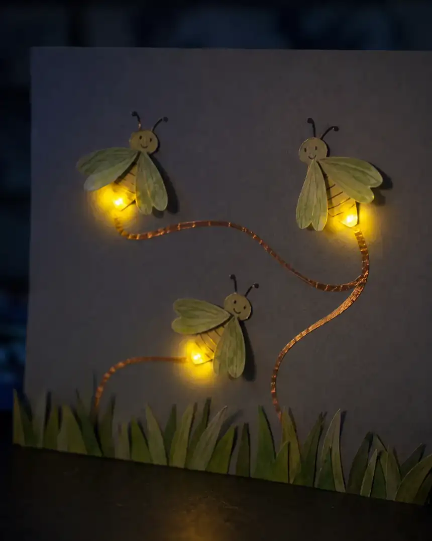 Vagalumes de papel acesos por pequenas luzes e trilhas de cobre